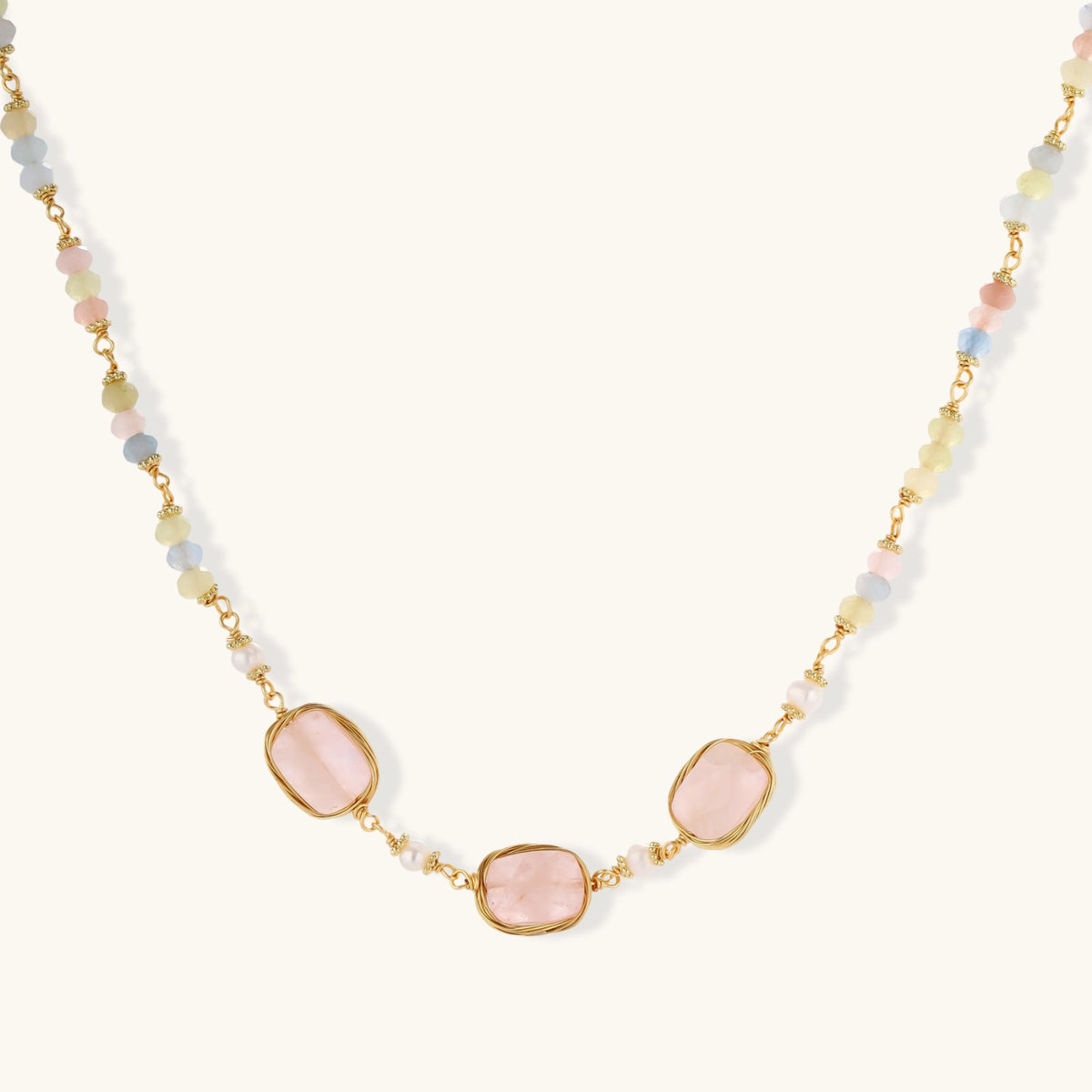 Gold necklace with three rose quartz stones, multicolor pastel beads, and pearl accents on white background.