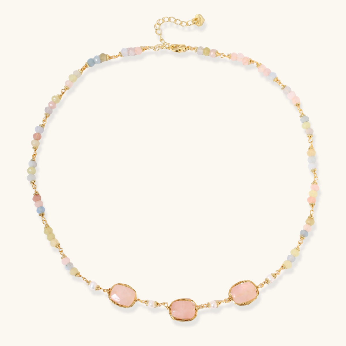 Gold necklace with three rose quartz stones, multicolor pastel beads, and pearl accents on white background.