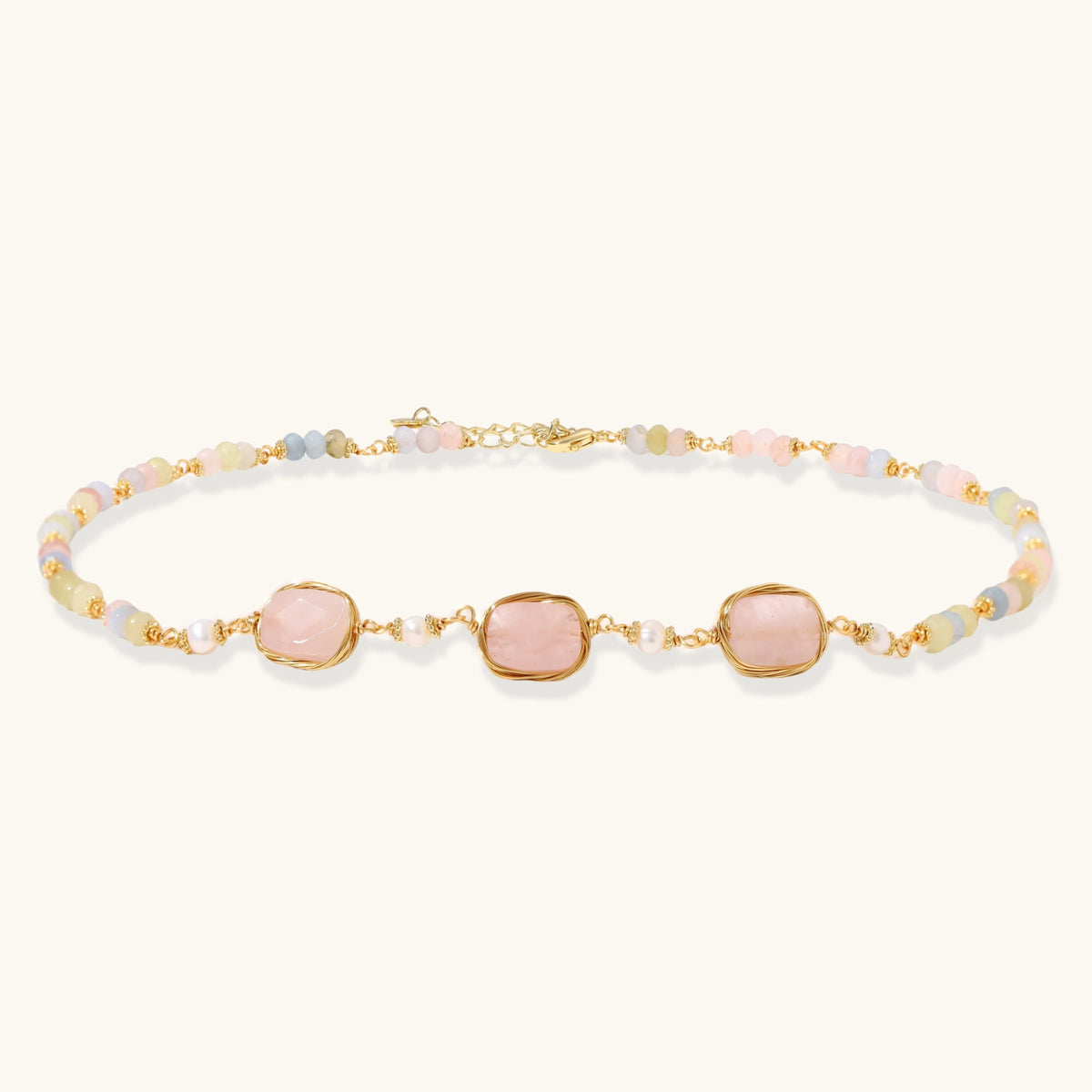 Gold necklace with three rose quartz stones, multicolor pastel beads, and pearl accents on white background.
